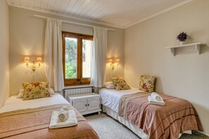 A bedroom with two beds, a window with curtains, wall-mounted lamps, and a small shelf with a plant.