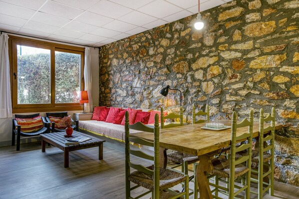 Una habitación con pared de piedra, muebles de madera, una ventana con cortinas y vistas a árboles.