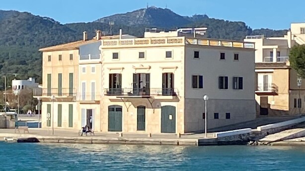 Un bâtiment situé sur la côte, doté d’un balcon, une personne qui passe, et une montagne en arrière-plan.