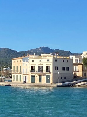 A coastal building with a balcony, a person walking by, and a mountain in the background.