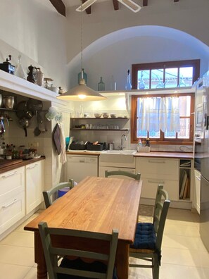 A kitchen with a wooden table and chairs, a hanging light fixture, and a window with curtains.
