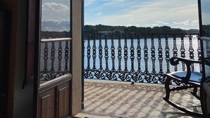 Une porte ouverte donnant sur un balcon avec vue sur une étendue d’eau et une côte lointaine.