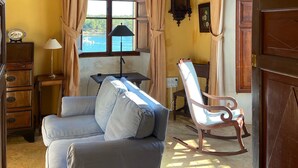 Une pièce comprenant un canapé, un fauteuil à bascule, une armoire en bois, une lampe, une horloge et une fenêtre avec des rideaux.