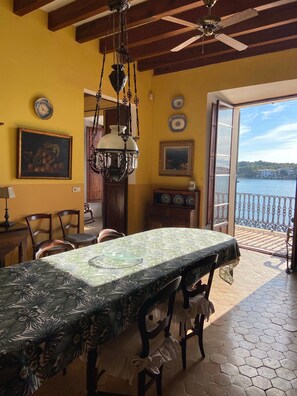 A dining area with a table set for four, a chandelier, and a view of a body of water through an open door.