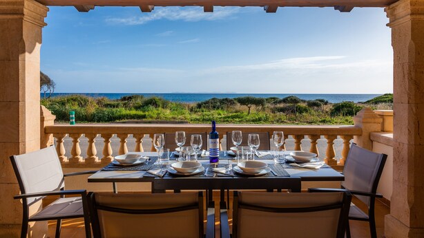 Une table dressée pour deux personnes, avec vue sur la mer, une bouteille de vin et un verre d’eau.