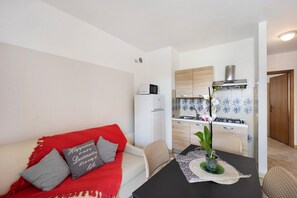 A compact living space with a kitchenette, a dining area with a table and chairs, and a sofa with cushions.