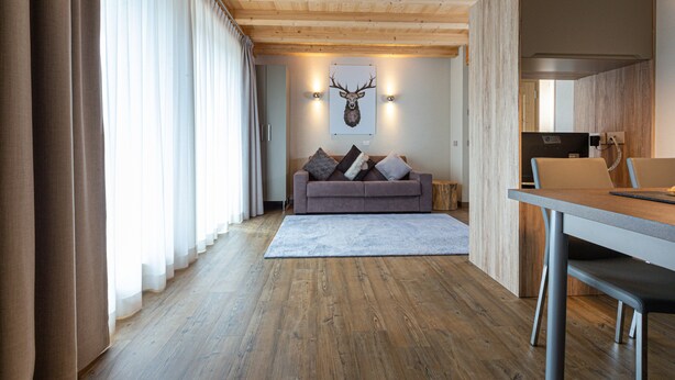 A modern interior with a wooden ceiling, a sofa with cushions, a dining table, and a mounted deer head on the wall. - Apartment 'Sant'Antoni Plan' with Mountain View, Shared Terrace and Wi-Fi (Livigno)