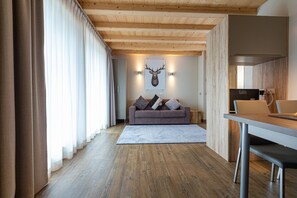 Ein modernes Interieur mit Holzbalkendecke, einer Couch mit Kissen, einem Esstisch und einem aufgehängten Hirschgeweih an der Wand.
