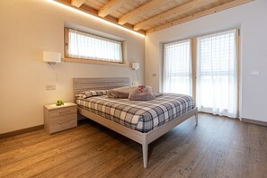 Ein Schlafzimmer mit einem Holzbett, Nachttischen, einem Beistelltisch und einem Fenster mit Vorhängen.