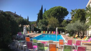 Una piscina con sillones y sombrillas de colores, rodeada de árboles y un patio de piedra.