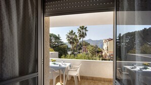 Un balcón con mesa y sillas, vista a palmeras y un edificio al fondo.