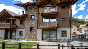 A multi-story building with balconies, stone facade, and a clear sky. - Apartment 'Sant'Antoni Fontana' with Mountain View, Shared Terrace and Wi-Fi (Livigno)