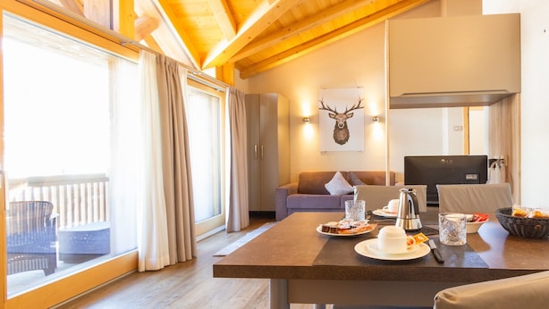 A cozy room with a dining table, a sofa, a TV, and a wall-mounted deer head decoration. - Apartment 'Sant'Antoni Fontana' with Mountain View, Shared Terrace and Wi-Fi (Livigno)