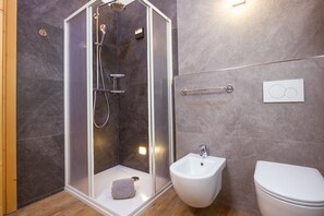 A modern bathroom with a glass-enclosed shower, a bidet, and a toilet.