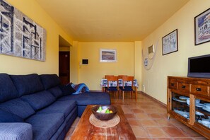 A living room with a sofa, a coffee table with fruit, a TV, and a dining area with chairs and a table.