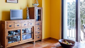 Ein Holzkasten mit Schubladen und Regalen, ein kleiner Fernseher und ein Fenster mit Blick auf Bäume.