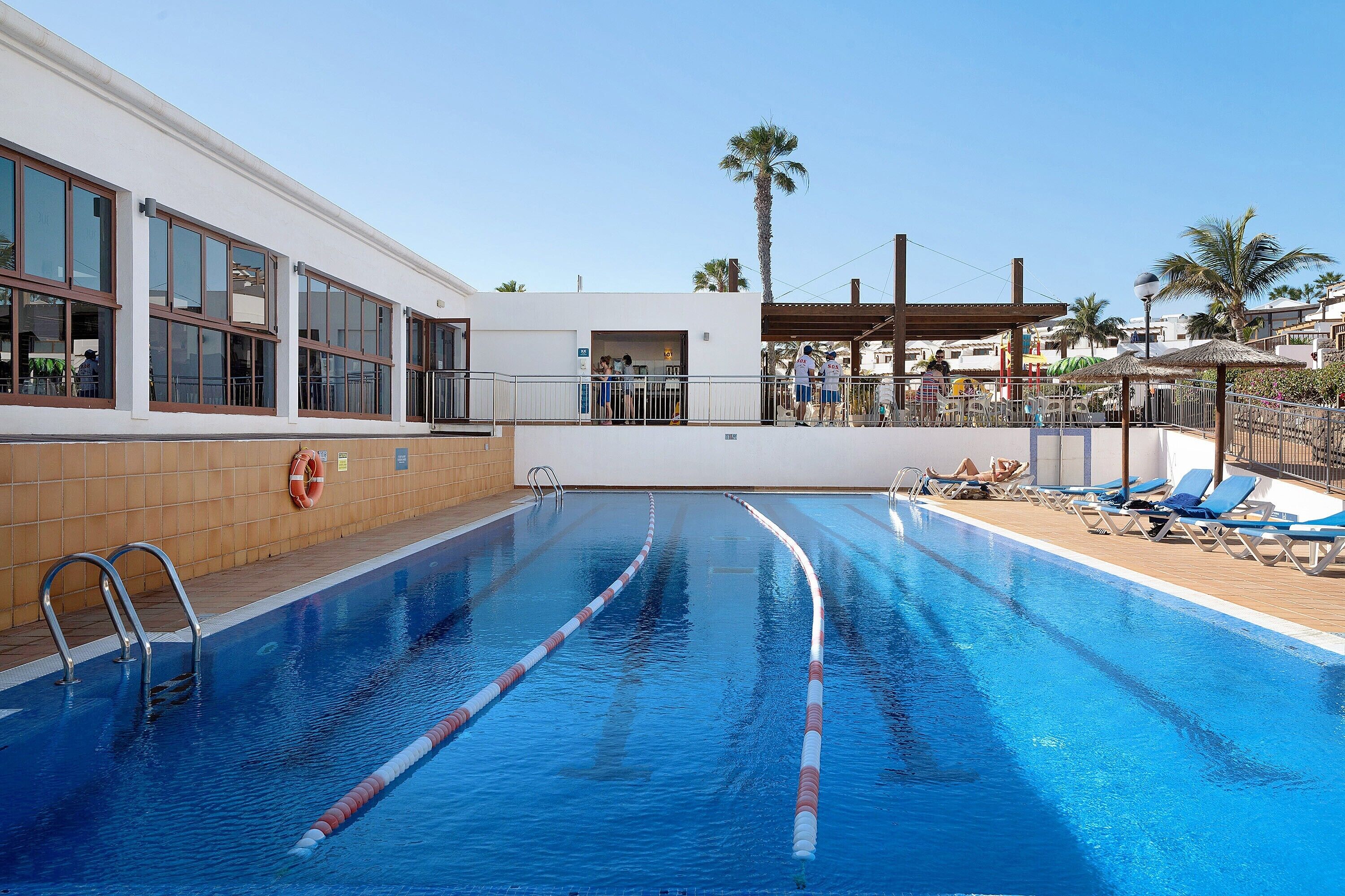 Une piscine avec des couloirs clairement délimités, un poste de surveillance pour les sauveteurs et des chaises longues.