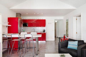 A modern kitchen with red cabinets, a white dining table with four chairs, and a black sofa with a striped pillow.