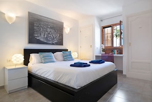A bedroom with a bed, nightstands, a wall-mounted light fixture, a window, and a door.