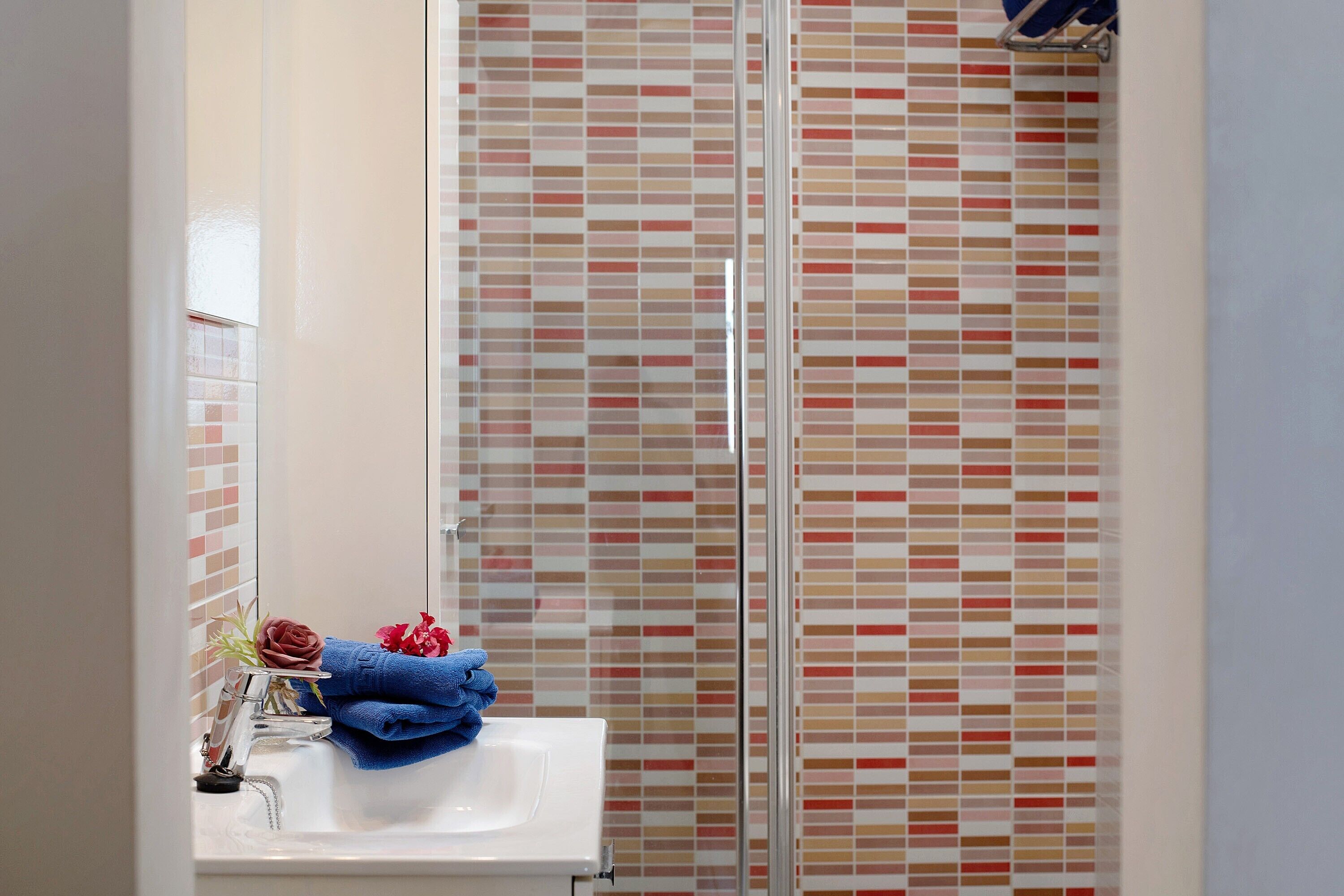 A bathroom with a glass shower enclosure, a sink with a towel, and a mirror.