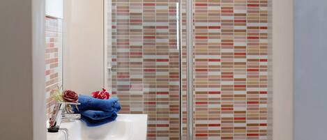 A bathroom with a glass shower enclosure, a sink with a towel, and a mirror.
