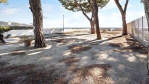 A sandy outdoor area with trees, a potted plant, and a metal fence. - Apartment Orizzonte 9 A with Shared Garden & Wi-Fi (Diano Marina)