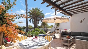 A patio with a table set for dining, chairs, a sofa, and a pergola.