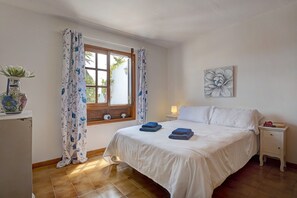 Une chambre à coucher avec un lit, une table de chevet, une lampe, un vase avec des fleurs et une fenêtre avec des rideaux.