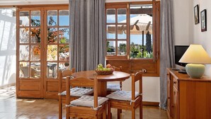 A dining area with a wooden table, chairs, a fruit basket, and a television on a wooden cabinet.