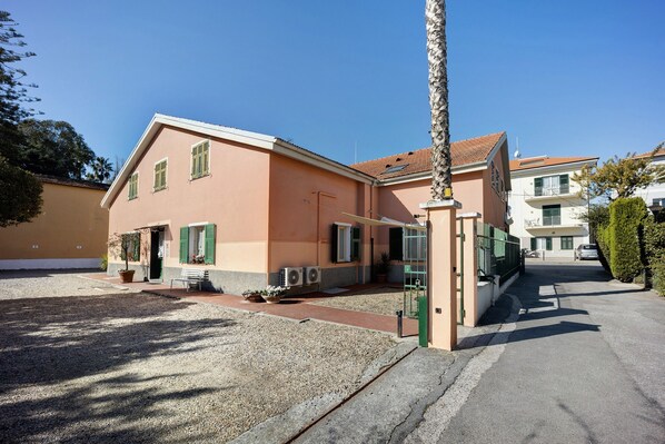 A two-story building with a flat roof, a gravel driveway, and a small garden area with a bench and potted plants.