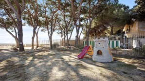 A playground with a slide and climbing structure, surrounded by trees and a fence.
