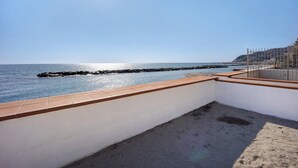 A balcony with a view of the sea, a sandy area, and a metal railing.