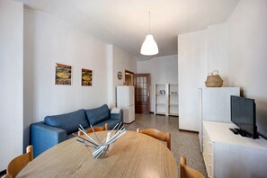 A compact living space with a dining table, blue sofa, and a TV on a cabinet.