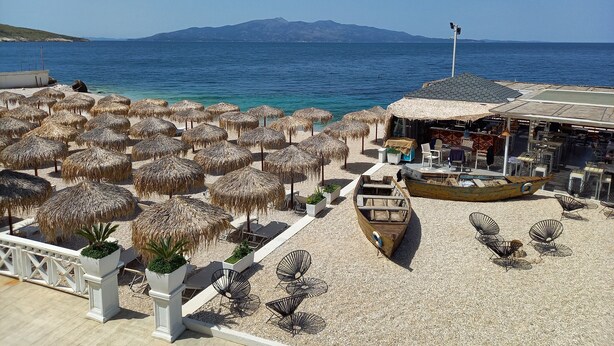 Un espace aménagé sur la plage, avec des parasols en chaume, des chaises longues et un bateau en bois.