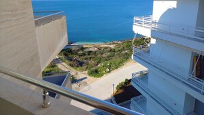 Un immeuble de grande hauteur doté de balcons qui offrent une vue sur une zone côtière, avec des eaux d’un bleu limpide et un paysage rocheux.