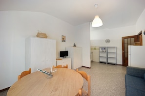 Une pièce comprenant une table ronde en bois, deux chaises, un meuble blanc, un téléviseur, une petite étagère et un canapé bleu.
