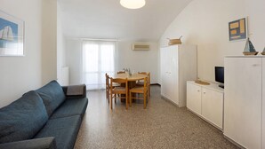 A living room with a sofa, a dining table with chairs, a TV on a cabinet, and a ceiling light.