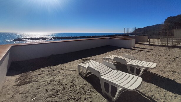 A beach with a sunlit sky, a rocky shoreline, and white plastic chairs.