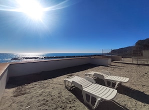 Une plage avec un ciel ensoleillé, une côte rocheuse et des chaises en plastique blanches.