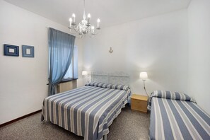 Una camera da letto con due letti, un lampadario, una finestra con tende e un comodino con una lampada.
