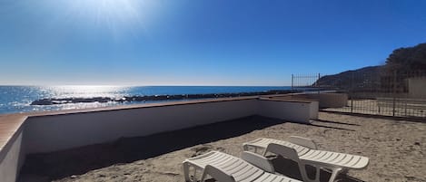 A beach with a sunlit sky, a rocky shoreline, and white plastic chairs.