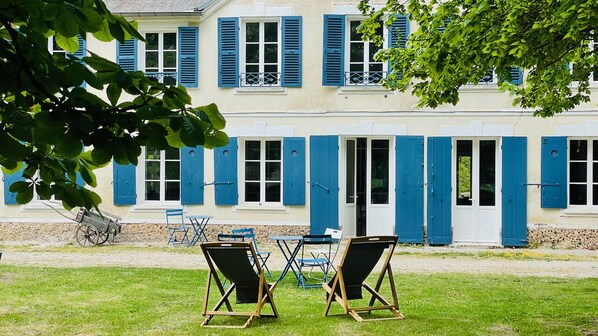 A building with blue shutters and a door, a bicycle, and two lawn chairs in the foreground.