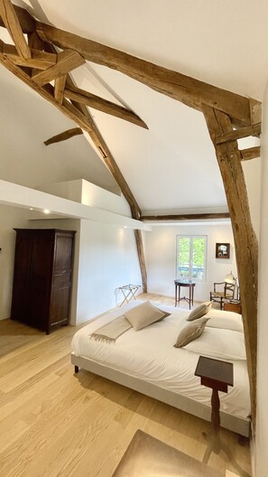 A bedroom with a sloped ceiling, a bed with pillows, a wooden wardrobe, and a window with a view.
