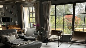 Ein geräumiges Wohnzimmer mit grauem Sofa, einem Couchtisch und einem großen Fenster mit Blick auf Grünflächen.