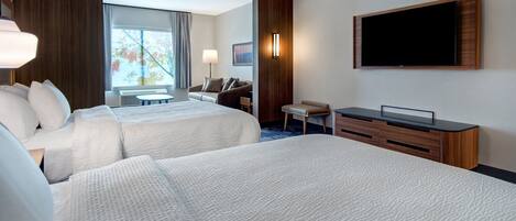 A hotel room with two beds, a desk, a TV, and a window with a view of trees.