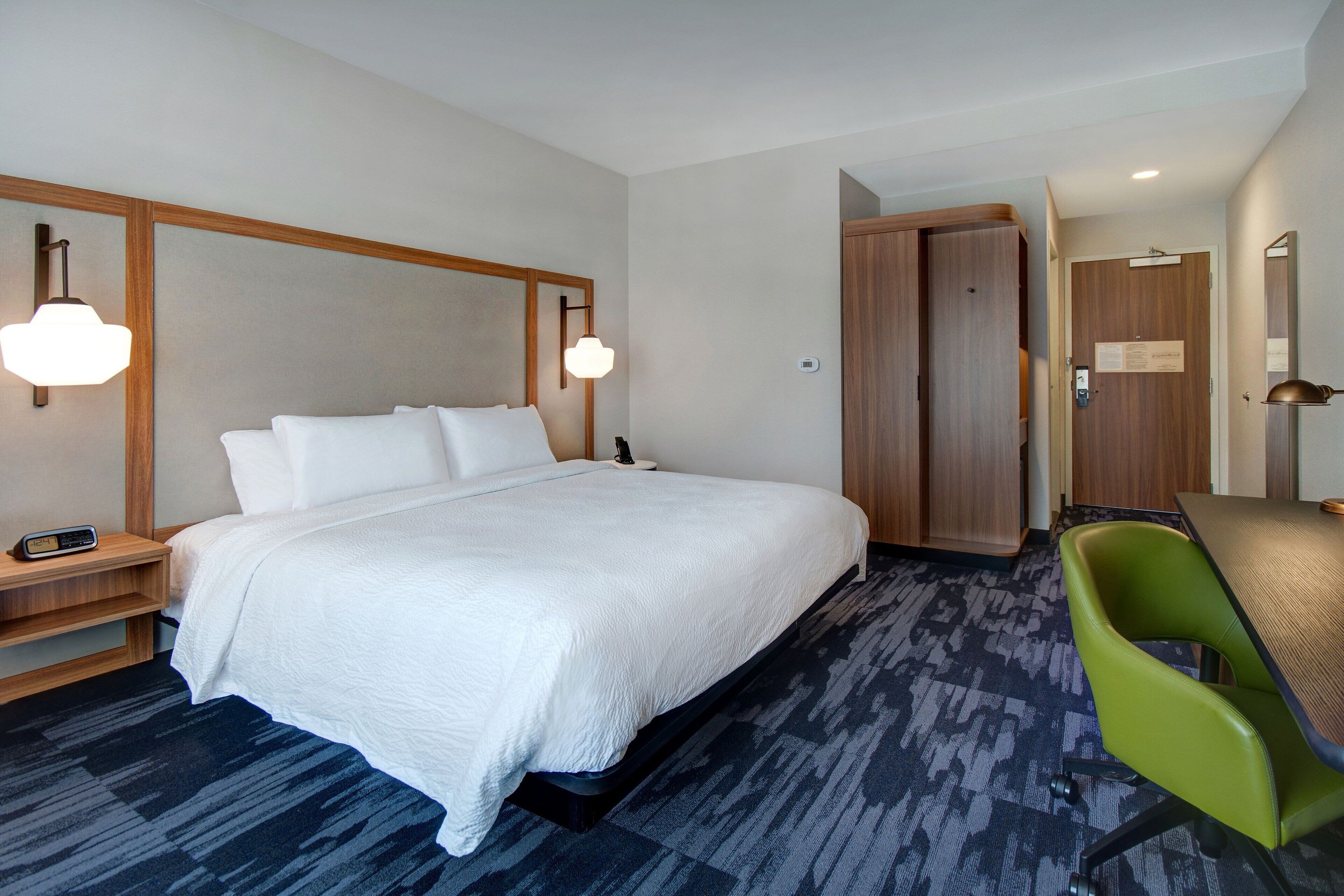 A hotel room with a large bed, a desk, a green chair, and a wooden wardrobe.