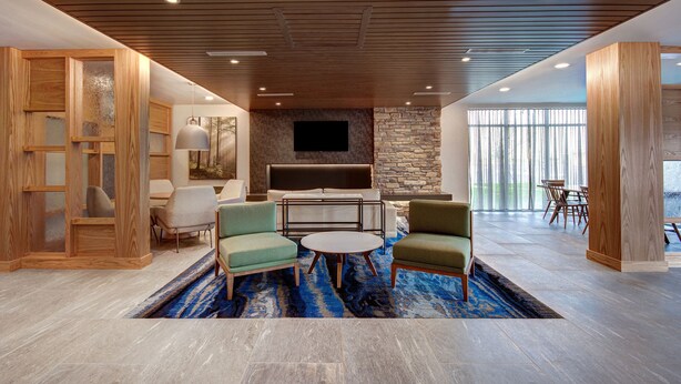 A modern living room with a stone fireplace, wooden furniture, and a large TV. - Fairfield by Marriott Inn & Suites Rochester Hills (Rochester)
