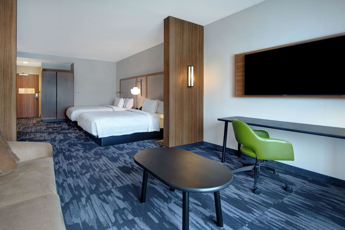 A hotel room with a bed, a desk, a green chair, and a flat-screen TV.