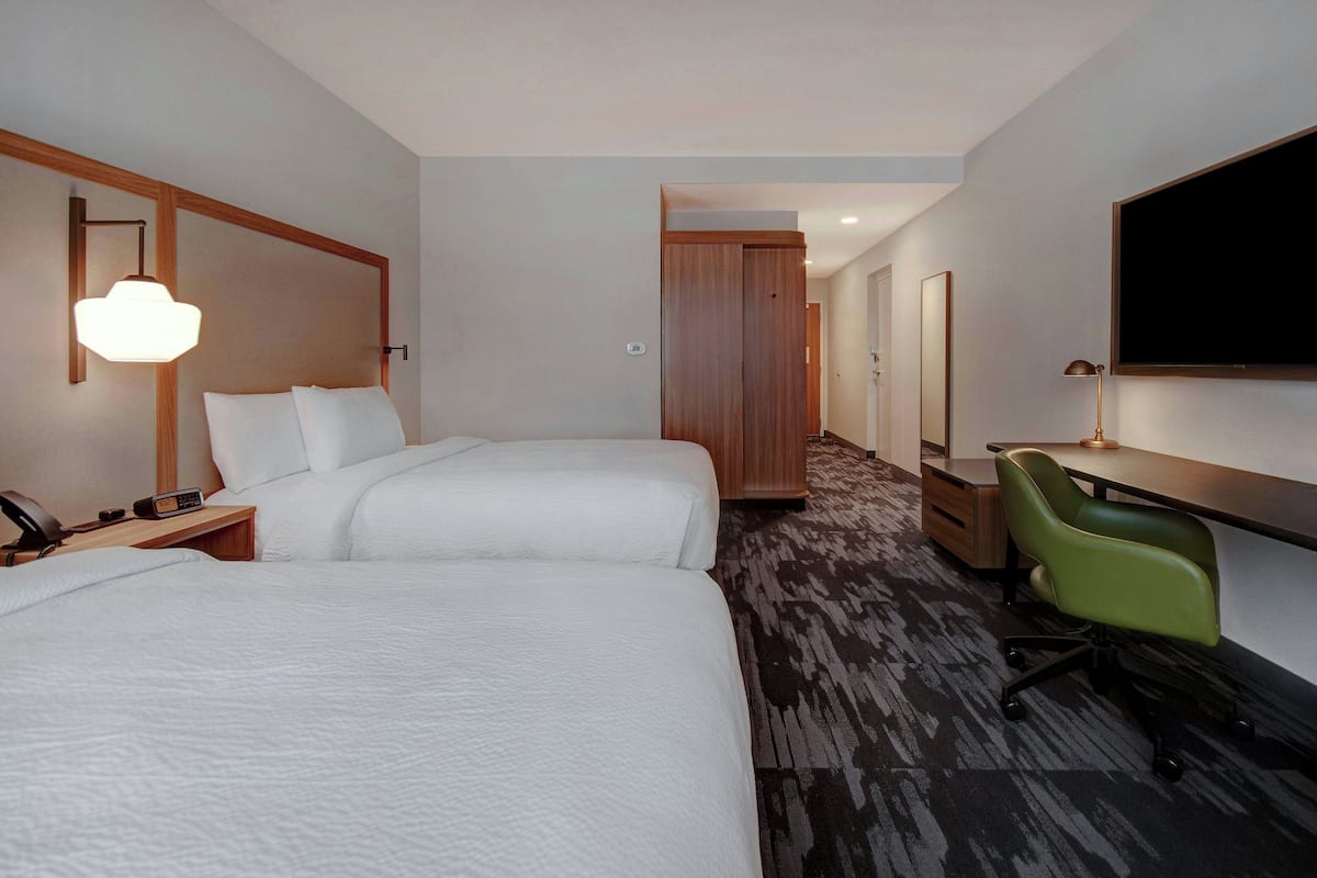 A hotel room with two beds, a desk with a chair, a TV, and a wardrobe.