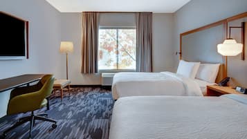 A hotel room with two beds, a desk, a chair, a lamp, and a window with curtains.